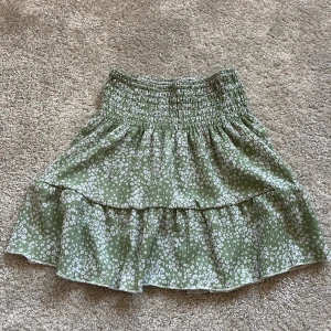 Grön blommig kjol från Gina Tricot - Söt grön kjol med blommigt mönster från Gina Tricot. Kjolen har en volangdetalj och en elastisk midja för en bekväm passform. Perfekt för en somrig look! 💕