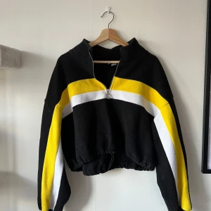 Fleecetröja med dragband - svart tröja med gula och vita ränder.