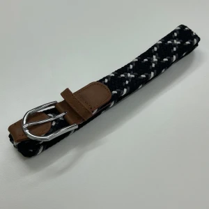 Svart och vitt flätat bälte - Snyggt flätat bälte i svart och vitt med bruna skinn-detaljer och ett silverfärgat spänne. Perfekt för att ge en stilren touch till din outfit.