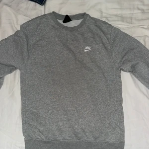 Grå sweatshirt från Nike - Säljer en klassisk grå sweatshirt från Nike med rund halsringning och det ikoniska Nike-loggan på bröstet. Tröjan har långa ärmar och ribbade muddar vid ärmslut och nederkant. Perfekt för en avslappnad stil.