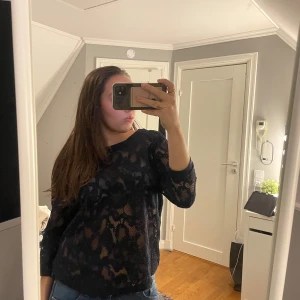 Svart spetsmönstrad tröja från Lindex - Säljer en svart spetsmönstrad tröja från Lindex. Tröjan har en luftig design med trekvarts ärmar och ribbade kanter. Perfekt för att lägga till en touch av elegans till din outfit. Är i strl L men passar mig som är S/M🖤