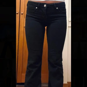 Svarta bootcut jeans - Snygga svarta bootcut jeans med låg midja och klassisk femficksdesign. Perfekta för en avslappnad stil. De har en dragkedja och knapp framtill.