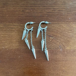Silvriga örhängen med kedjor och koner - Snygga silvriga örhängen med hängande kedjor och konformade detaljer. Perfekta för att ge en edgy touch till din outfit. De har en modern design med tre koner per örhänge som hänger från små kedjor. Använd 1 gång