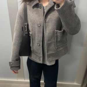 Grå ulljacka med knappar - Säljer en  grå ulljacka med knappar framtill och stora fickor. Jackan har långa ärmar med knappar vid ärmsluten och en klassisk krage. Perfekt för kyligare dagar men även över linne i vårsolen💗