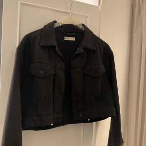 Svart croppad jeansjacka  - Säljer en svart croppad jeansjacka från Ginatricot. Jackan har långa ärmar och knappar framtill samt på bröstfickorna. 