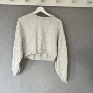 Grå croppad sweatshirt - Säljer en stilren grå croppad sweatshirt med långa ärmar. Perfekt för en avslappnad look. Tröjan har en rund halsringning och ribbade muddar vid ärmslut och nederkant.
