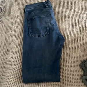 Mörkblå jeans från Replay - Snygga mörkblå jeans från Replay med klassisk femficksdesign och knappgylf. Perfekta för en stilren look. Märkeslogga på bakfickan ger en extra touch.