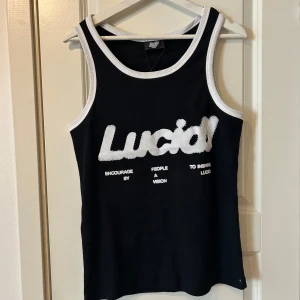 Svart ribbad linnetopp från Lucid - Säljer en svart ribbad linnetopp från Lucid med vit text och kantdetaljer. Toppen har ett tryck med texten 'Lucid' och är perfekt för en avslappnad stil.