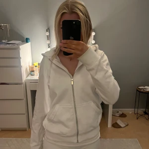 Vit hoodie med dragkedja - Säljer en stilren vit hoodie med dragkedja och fickor framtill. Den har en bekväm passform och en praktisk huva. Använt 1 gång, har en liten liten fläck men går bort i tvätten.