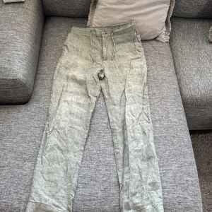 Gröna linnebyxor från These Glory Days - Snygga gröna linnebyxor från These Glory Days. Jätte fina överlag men en liten fläck på låret.       De har en avslappnad passform med knappar och dragkedja framtill. Perfekta för en stilren och bekväm look.