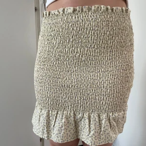 Beige/Gul blommig kjol med volang - Söt beige/gulaktig kjol med små blommor och volangdetalj längst ner. Kjolen har en tight passform och är perfekt för varma dagar. Den elastiska midjan ger en bekväm känsla samt gör så den passar flera storlekar - egensydd, aldrig använd  @sytanten_ (Instagram)