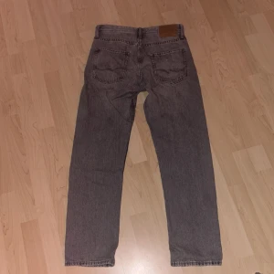 Grå jeans från Jack & Jones (Relaxed/Chris) - Snygga grå jeans från Jack & Jones med klassisk femficksdesign. De har en knappgylf och en läderpatch på baksidan av midjan. Perfekta för en avslappnad stil. Köpta för ungefär en månad sen. Använd 2-3 gånger.