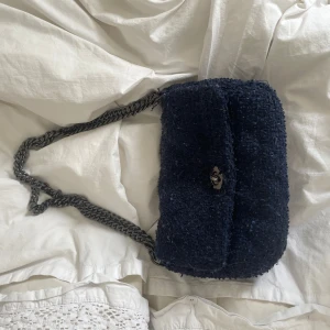 Beck sondergardMörkblå axelväska med kedja - Snygg mörkblå axelväska med en stilren kedja som axelrem. Väskan har en mjuk och fluffig textur vilket ger den en unik look. Perfekt för att ge din outfit en extra touch.