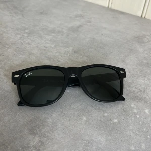 Svarta solglasögon från Ray-Ban - Klassiska svarta solglasögon från Ray-Ban med en tidlös design. De har en robust plastbåge och mörka linser som ger ett stilrent intryck. Perfekta för soliga dagar och en snygg accessoar till din outfit.