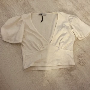 Vit omlottopp från Pigalle - Säljer en stilren vit omlottopp från Pigalle. Toppen har korta ärmar och en v-ringad design som ger en elegant look. Perfekt för både vardag och festliga tillfällen. Materialet är mjukt och bekvämt.