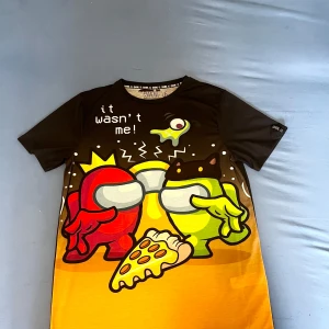 Svart och orange Among Us t-shirt - Cool t-shirt med Among Us-tema i svart och orange. Framsidan har ett färgglatt tryck med karaktärer och texten 'it wasn't me!'. Perfekt för fans av spelet som vill sticka ut.