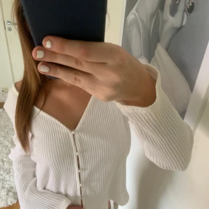 Vit ribbad kofta - Säljer en stilren vit ribbad kofta med v-ringning och knappar framtill. Perfekt för en avslappnad look. Passar bra till både jeans och kjol.
