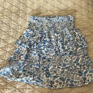 Blommig kjol från BikBok - Söt blommig kjol från BikBok i blått och vitt. Kjolen har en volangdetalj och ett elastiskt midjeband för en bekväm passform. Perfekt för varma dagar!