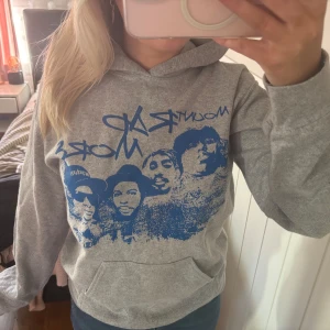 mount rap more hoodie - Säljer en grå hoodie med ett stort blått tryck av ansikten på framsidan. Tröjan har en klassisk känguruficka och en bekväm huva. Perfekt för en avslappnad stil.