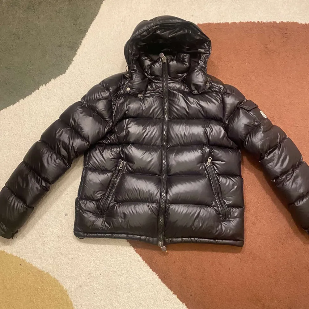 Säljer en snygg svart dunjacka från Moncler med huva och dragkedja. Jackan har en quiltad design och två fickor med dragkedjor. Perfekt för kalla dagar!. Takit.