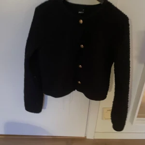 Mörk blå kofta från Gina Tricot - Säljer en mörkblå tröja från Gina Tricot med dekorativa knappar i guld. Tröjan har en mjuk och texturerad yta och långa ärmar. Perfekt för att hålla sig varm och stilren.i strl xs ursprungs pris runt 400.Inte använd mycket.