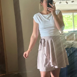 Beige omlottkjol från NLY Trend - Säljer en superfin beige omlottkjol från NLY Trend i storlek 38. Kjolen har knytband i midjan och en lätt, flowy känsla som ger en avslappnad men ändå chic look. Perfekt för varma dagar och enkel att styla med en enkel topp.