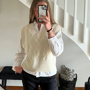 Vit finstickad väst med flätmönster - Snygg vit stickad väst med klassiskt flätmönster och v-ringning. Perfekt att bära över en skjorta för en stilren outfit.🥰
