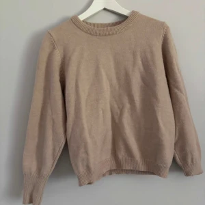 Beige stickad tröja från Dazy - En stilren beige stickad tröja från Dazy i storlek M. Tröjan har rund halsringning, ribbade muddar vid ärmslut och nederkant samt långärmad passform. Materialmix av akryl, polyamid och polyester gör den både mjuk och lätt att bära.