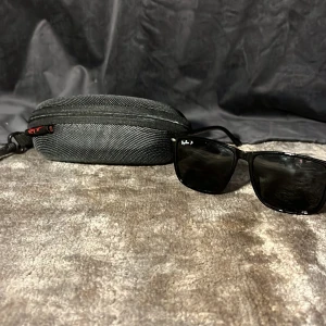  Ray-Ban solglasögon Wayfarer - Snygga svarta Ray-Ban Wayfarer solglasögon med klassisk fyrkantig form och mörka glas. Kommer med ett robust svart fodral med dragkedja och Ray-Ban-logga. Perfekta för att ge en cool vibe till din stil.
