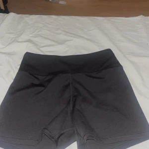 Svarta träningstights-shorts från Move - Svarta, tighta träningstights-shorts från Move med hög midja. Snygg och enkel design utan mönster, perfekta för gymmet eller löprundan. Materialet är stretchigt och följsamt för maximal rörelsefrihet.