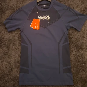 Mörkblå t-shirt från YoungLA - Snygg mörkblå t-shirt från YoungLA med coolt grafiskt mönster i svart och vit logga på bröstet. T-shirten har korta ärmar och är tillverkad i ett stretchigt material som passar perfekt till träning eller chill. Modern passform och sportig vibe.