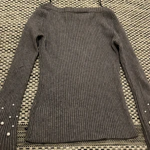 Grå ribbad tröja med pärlor Bodyflirt - Supersnygg grå ribbstickad tröja från Bodyflirt i storlek XS. Långärmad modell med tight passform och dekorativa pärlor på ärmsluten som ger en extra touch. Perfekt till jeans eller kjol för en trendig look.
