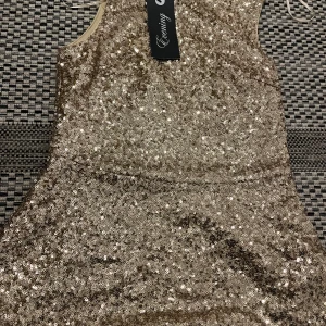 Glittrig guldklänning från Amisu - Supersnygg kort glittrig blus från Amisu i guld med massor av paljetter. Ärmlös modell med rund halsringning och figurnära passform. Perfekt för dig som vill sticka ut och glänsa på nästa fest!