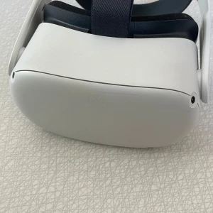 Meta Quest 2 VR-headset - Säljer ett Meta Quest 2 VR-headset i stilren vit färg med svarta detaljer. Justerbart huvudband i textil och mjuk vaddering för extra komfort. Perfekt för att dyka in i VR-världen och spela spel eller utforska nya upplevelser. 