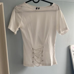 Vit topp med snörning från Vero Moda - Vit kortärmad topp från Vero Moda med cool snörningsdetalj framtill. Jag har sytt in midjan lite så den sitter lite tajtare. Tyvärr så har den två slitningar där fram som man lätt kan sy ihop.