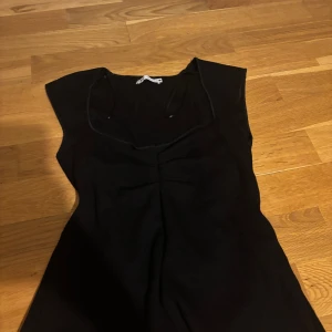Svart ärmlös topp från Zara - Säljer en svart, figurnära topp från Zara med snyggt rynkad detalj framtill. Toppen är ärmlös och har en mjuk, stretchig känsla som gör den bekväm att bära. Perfekt att styla med jeans eller kjol för en clean look.