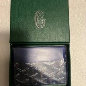 Blå Goy4rd plånbok med mönster - Säljer en blå plånbok från Goy4rd med deras ikoniska grafiska mönster i vitt och grått. Plånboken är i smidig modell med flera kortfack och har Goy4rd Paris tryckt på framsidan. Kommer i original grön ask med silverlogga. Pris kan diskuteras. Nyskick.