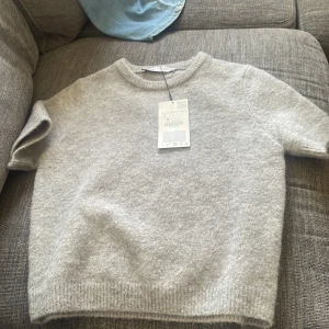 Grå stickad tröja från Zara - Supermjuk grå stickad tröja från Zara i storlek S. Tröjan har korta ärmar, rund halsringning och ribbade kanter. Aldrig använd! Väldigt populär tröja, stickad T-shirt🩷 original pris 329kr säljer för mycket billigare!