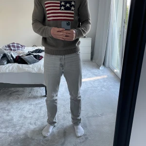 Grå stickad tröja Selected Homme - Snygg grå stickad tröja från Selected Homme med amerikansk flagga framtill i rött, vitt och blått. Tröjan har rund hals, ribbade muddar och lång ärm. Perfekt för dig som gillar en klassisk men ändå cool look.
