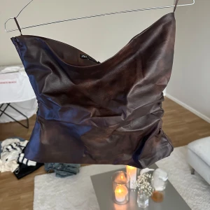 Brun tubtopp i skinnimitation från Zara - Snygg brun tubtopp från Zara i skinnimitation med lätt rynkade sidor. Toppen har en cool, glansig finish och bandeau-modell som sitter tight över bröstet. Perfekt att styla med jeans eller kjol för en trendig look.🤎