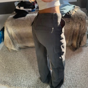 Mörkgrå cargopants med raka ben - Säljer ett par mörkgrå cargopants med raka ben och flera fickor på sidorna. Byxorna har normal passform och midwaist, perfekta för en chill och avslappnad stil. Materialet känns slitstarkt och passar till många olika outfits.