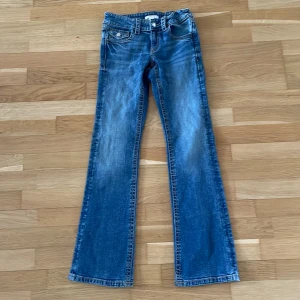 Blå bootcut jeans från Gina Tricot - Snygga blå jeans från Gina Tricot i modell bootcut. Jeansen har klassisk femficksdesign med lock på fickorna och silverfärgade knappar. Materialet är jeans med tydliga kontrastsömmar och en lätt tvättad look.