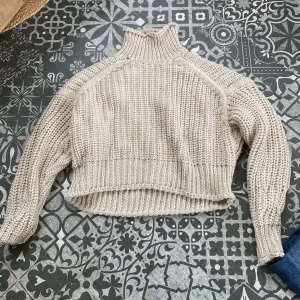 Beige stickad polotröja - Säljer en chunky beige stickad polotröja med hög krage och lång ärm. Tröjan har en loose fit och är ribbstickad vid muddar och nederkant. Ett litet hål i kragen. ☀️
