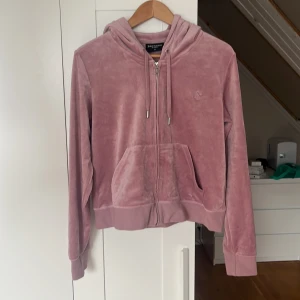 Rosa velour hoodie från Juicy Couture - Säljer en ljusrosa hoodie från Juicy Couture i mjuk velour med dragkedja framtill och huva med snörning. Klassisk logga broderad på bröstet och två fickor. Perfekt för en chill och trendig look. 210 + frakt 
