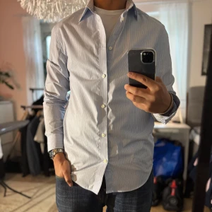 Blåvit randig skjorta från H&M - Snygg blåvit randig skjorta från H&M i regular fit. Skjortan har klassisk krage, långa ärmar med manschett och knäppning framtill. Perfekt till jeans eller chinos för en clean look. Tillverkad i mjuk bomull som känns skön mot huden.
