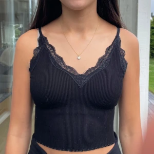 Svart linne - Säljer en svart croppad linnetopp med smala axelband och v-ringning. Toppen är ribbad och har fina spetsdetaljer längs urringningen. Perfekt för sommaren.