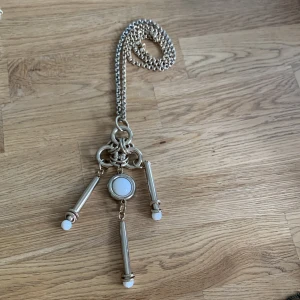 Unikt silver/guldfärgat halsband med hängen - Snyggt halsband i guld/silverfärg med tre avlånga hängen och en rund vit detalj i mitten. Kedjan är grov och ger ett coolt intryck. Hängena har vita toppar som matchar den runda detaljen. Perfekt för dig som gillar statement-smycken.
