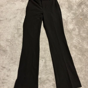 Svarta kostymbyxor från BikBok, stl 36 - Snygga svarta kostymbyxor från BikBok i storlek 36. Byxorna har diskreta vita ränder, raka ben och bälteshällor. Materialet känns mjukt och följsamt.