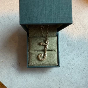 Guldigt halsband Maria Nilsdotter J - Snyggt halsband från Maria Nilsdotter med ett guldigt J-hänge. Kedjan är tunn och halsbandet kommer i originalask. Nypris 2150kr. 