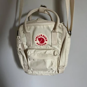 Handväska på fjällräven - En beige handväska/axelbandsväska från Fjällräven. Den har en liten framficka, ett stort huvudfak och sen ett fak längst bak. 